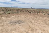 a dirt and field with mountains in the distance, some bushes and dirt covered ground