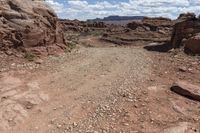 dirt road running through a canyon in the desert with mountains behind it on a cloudy day