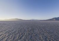 a lone person walking in a very large desert area with hills behind them and the ocean in the foreground