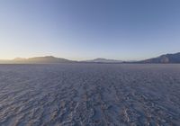 a lone person walking in a very large desert area with hills behind them and the ocean in the foreground