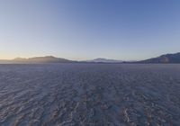 a lone person walking in a very large desert area with hills behind them and the ocean in the foreground
