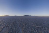 a lone person walking in a very large desert area with hills behind them and the ocean in the foreground