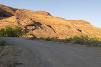 a dirt road leading to the top of a hill near a rock formation and plants