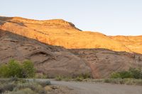 a person riding a bike down a dirt road with cliffs in the background at dusk