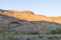 a person riding a bike down a dirt road with cliffs in the background at dusk