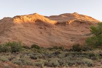 a person riding a bike down a dirt road with cliffs in the background at dusk