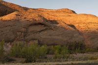 a person riding a bike down a dirt road with cliffs in the background at dusk