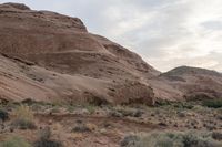 a dirt and brush area next to a large mountain side with some very tall rocks