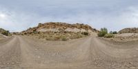 a car driving on a dirt road through the desert with a small mound in the distance