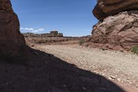 a dirt road in a desert area with large rock formations and a building on the other side