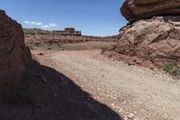 a dirt road in a desert area with large rock formations and a building on the other side