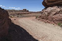 a dirt road in a desert area with large rock formations and a building on the other side