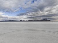 a man walks across an empty salt flat landscape with mountains in the distance and a bright blue sky