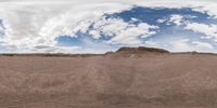 a fisheye view of a desert and sky with clouds above it to the right