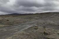 an open desert with an empty road and a mountain behind it in the distance, there is clouds