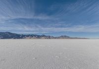 a very large flat desert with footprints in it in front of mountains in the distance