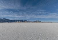 a very large flat desert with footprints in it in front of mountains in the distance