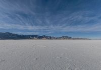 a very large flat desert with footprints in it in front of mountains in the distance