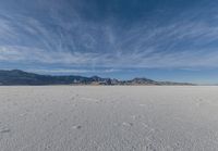 a very large flat desert with footprints in it in front of mountains in the distance