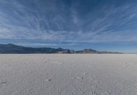 a very large flat desert with footprints in it in front of mountains in the distance