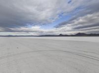 a lone horse is walking in the desert with snow on the ground and hills behind it