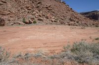 a dirt road through a desert plain with a mountain behind it and a clear blue sky in the background