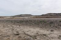 a man walking in the middle of a dirt field near hills and rocks with a sky