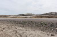 a man walking in the middle of a dirt field near hills and rocks with a sky