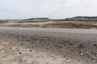 a man walking in the middle of a dirt field near hills and rocks with a sky