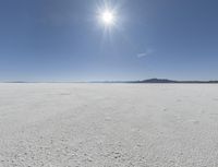 someone walks across an open desert plain, with the sun in the sky above them