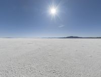 someone walks across an open desert plain, with the sun in the sky above them