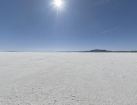 someone walks across an open desert plain, with the sun in the sky above them