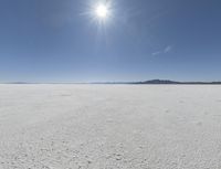 someone walks across an open desert plain, with the sun in the sky above them