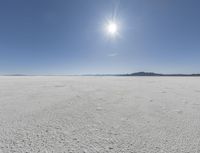 someone walks across an open desert plain, with the sun in the sky above them