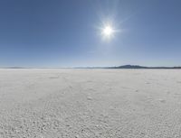 someone walks across an open desert plain, with the sun in the sky above them