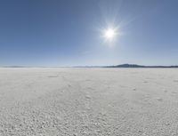 someone walks across an open desert plain, with the sun in the sky above them