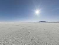 someone walks across an open desert plain, with the sun in the sky above them