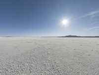 someone walks across an open desert plain, with the sun in the sky above them