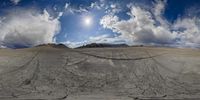 a desert area with cracked rocks and mountains under a partly cloudy sky, some clouds behind