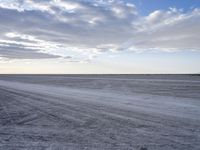 an empty dirt road winds through an empty field with clouds and a distant horizon on the horizon