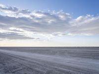 an empty dirt road winds through an empty field with clouds and a distant horizon on the horizon