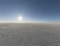 a wide shot of the desert with snow on it and sun glaring behind a blue sky