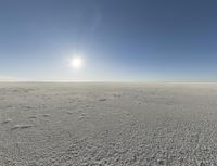 a wide shot of the desert with snow on it and sun glaring behind a blue sky