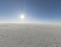 a wide shot of the desert with snow on it and sun glaring behind a blue sky