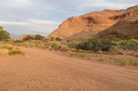 the dirt road in the desert is covered with rocks and trees in the distance are cliffs