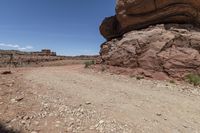 a small dirt road in the desert with rocks and plants along side and a big rock on top