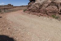 a small dirt road in the desert with rocks and plants along side and a big rock on top