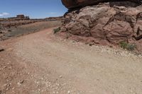 a small dirt road in the desert with rocks and plants along side and a big rock on top