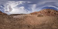 a panoramic view of desert area and large rocks under blue sky with clouds