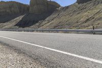 a biker riding down a street next to a canyon side highway with mountains and cliffs